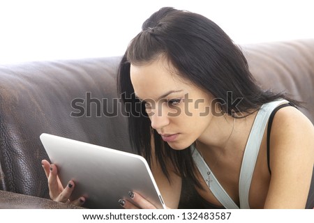 Young woman on a brown coach reading from a digital tablet.