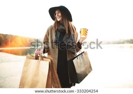 Attractive cute girl in with the shopping bags and warm drink in her hand