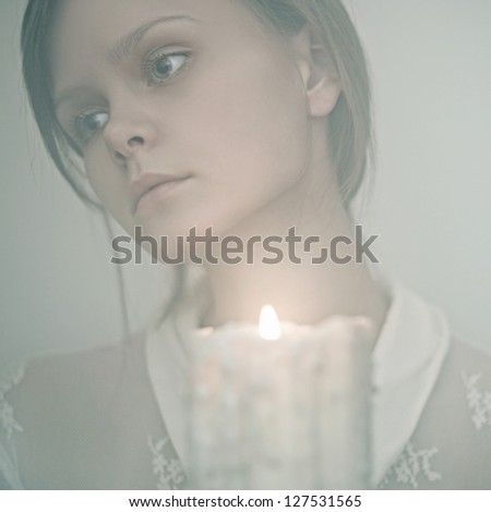 Young woman looking to a candle, mysterious photograph on a white background