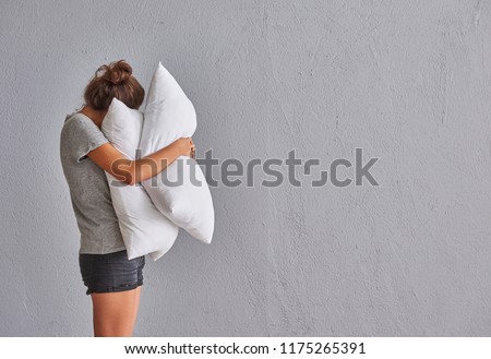 while girl hug a pillow in front of the grey wall. Girl is sleeping.