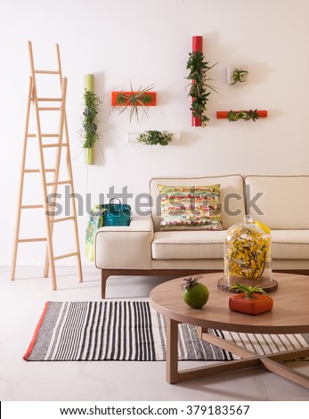 In the modern living room with comfortable sofas, natural wood staircase, flowering of modern wall decor