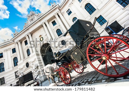 Wide-angle view of famous Hofburg Palace with traditional horse-drawn Fiaker carriages on a sunny day in Vienna, Austria