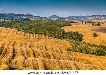 Rolling hills and harvest fields in golden evening light with famous Cappella della Madonna di Vitaleta and the old town of Pienza in the background, Val d\'Orcia, Tuscany, Italy