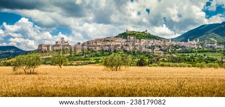 Panoramic view of the ancient town of Assisi with dramatic cloudscape and golden harvest fields, Umbria, Italy
