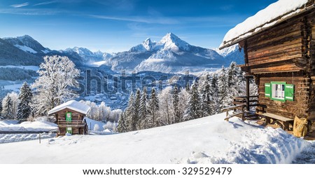 Panoramic view of beautiful white winter wonderland mountain scenery in the Alps with traditional mountain chalets on a cold sunny day with blue sky and clouds