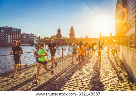 Group of female and male young active runners jogging outside in evening light at sunset in summer with retro vintage old Instagram style toned filter and lens flare sunlight effect in the background