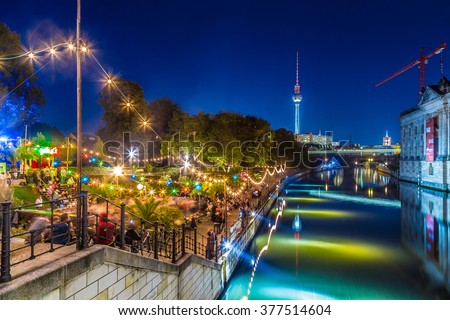 People dancing at summer Strandbar beach party near Spree river at historic Museum Island with famous TV tower in the background in twilight during blue hour at dusk, Berlin Mitte district, Germany