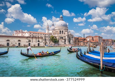 Beautiful view of traditional Gondolas on Canal Grande with historic Basilica di Santa Maria della Salute in the background on a sunny day with blue sky and clouds in Venice, Italy