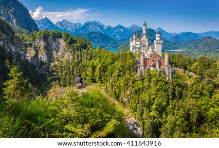 Young man sitting on a cliff enjoying the view on famous Neuschwanstein Castle, the 19th century Romanesque Revival palace built for King Ludwig II, in summer, Fussen, southwest Bavaria, Germany