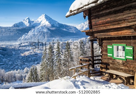 Beautiful view of scenic white winter wonderland mountain scenery in the Alps with traditional mountain chalet on a cold sunny day with blue sky and clouds