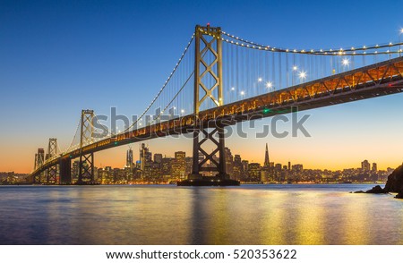 Classic panoramic view of famous Oakland Bay Bridge with the skyline of San Francisco in the background illuminated in beautiful twilight after sunset in summer, California, USA