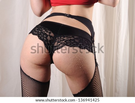 Beautiful buttocks of a woman wearing fishnet stockings, lace panties and suspenders lifting her red dress
