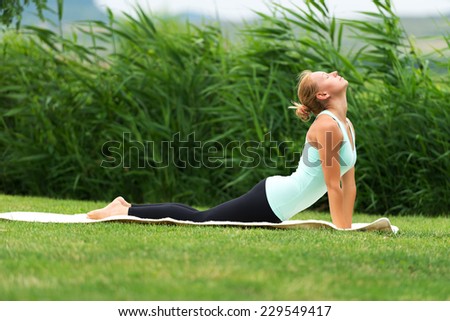 Yoga bhujangasana cobra pose by woman on green grass in the park