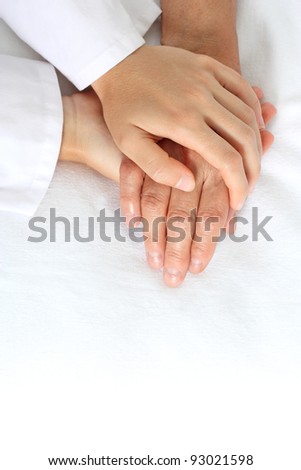 Woman holding senior woman's hand on bed