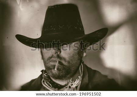 Old West Cowboy Smoker Close. An old west cowboy in a hat smoking a hand rolled cigarette, edited in vintage film style.
