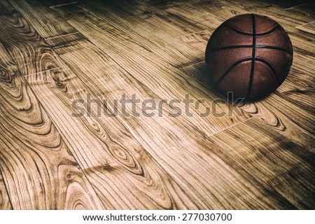 Basketball on Hardwood 2. A basketball laying on the ground of a hardwood court in a gymnasium.