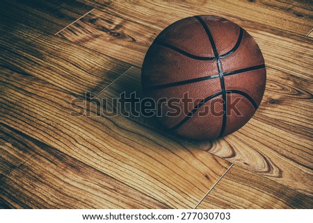 Basketball on Hardwood 1. A basketball laying on the ground of a hardwood court in a gymnasium.