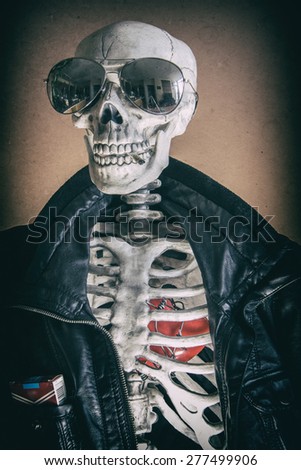 Cool Skeleton Smoker. A cool skeleton wearing a leather jacket and sunglasses, with cigarettes in his pocket and a smoke in his mouth. His heart visible in his ribcage. Edited in vintage film style.