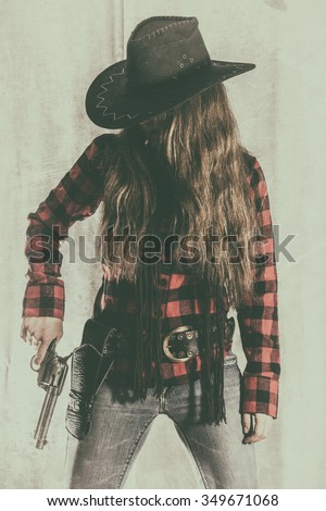 Cowgirl Gunslinger Holding Gun. Old west cowgirl gunslinger standing, holding peacemaker gun at her side, edited in vintage film style.