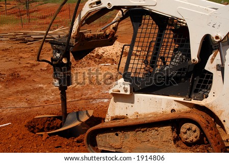 Construction Site, Small front end loader digging a hole with a big drill. Close up.