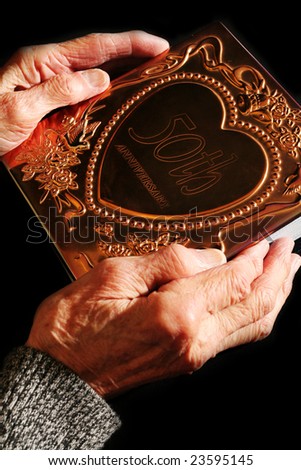 Elderly hand cherishing a photo-album from a 50th wedding anniversary celebration