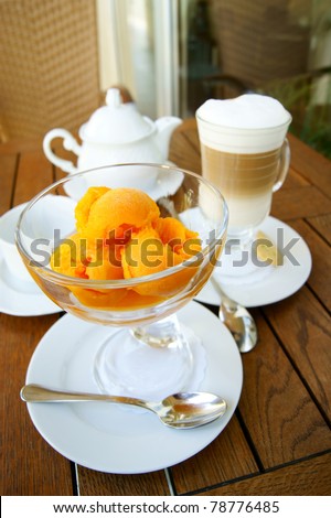 orange ice cream in a glass bowl and glass of coffee latte  on the background of the wooden table surface