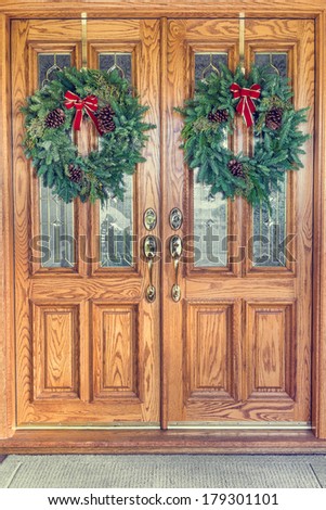 Two Christmas wreaths hanging from a double front door