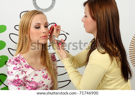 Professional makeup artist applying mascara on the eyebrows of a beautiful girl.