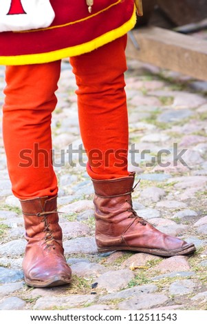 Legs of a man in red pants and  medieval leather boots on a carriageway
