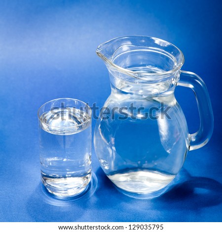 Glass of water and jug over blue background