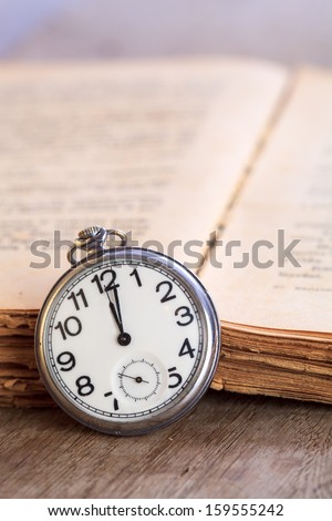 Pocket watch next to old opened book