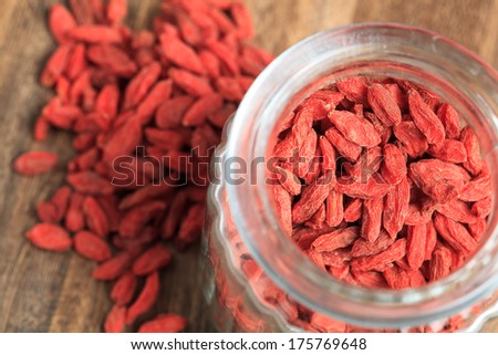 Goji berries and glass bowl closeup on brown wooden table. Shallow depth o field