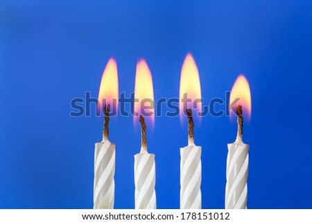 Four white birthday candles burning over blue background