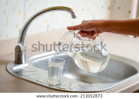 Hand pouring water into glass from jug on kitchen sink