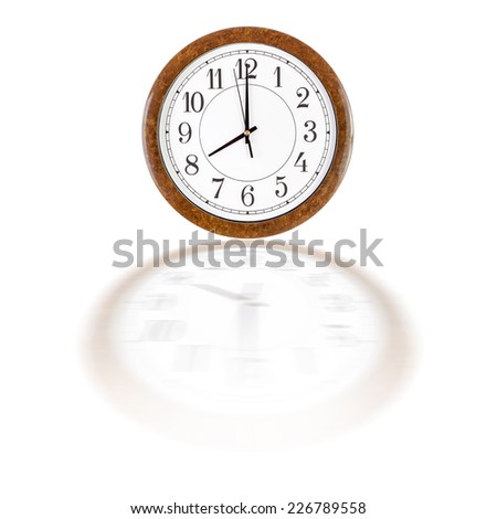 A white clock face in brown wooden frame showing eight o\'clock over white background with blurry reflection