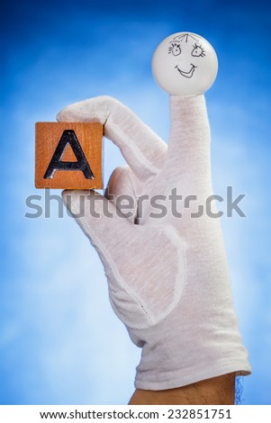 Finger puppet holding wooden cube with capital letter A over blue background
