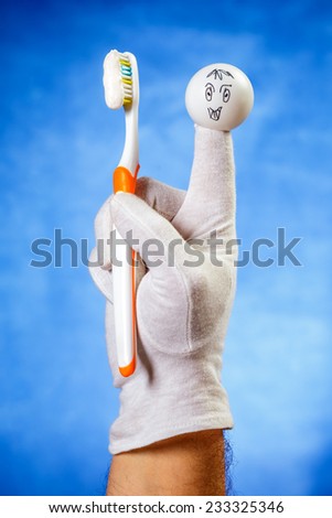 Happy finger puppet holding toothbrush with toothpaste over blue background