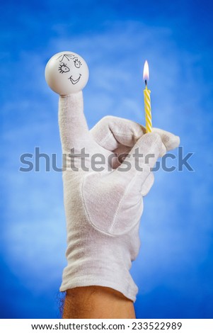 Burning birthday candle hold by girl finger puppet over blue background