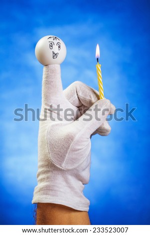 Burning birthday candle hold by white finger puppet over blue background