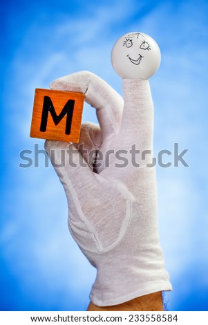 Finger puppet holding wooden cube with capital letter M over blue background