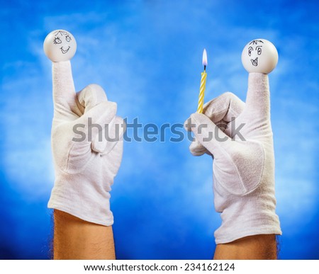 Happy finger puppet receiving burning candle from other smiling finger puppet over blue background