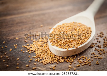 Wooden spoon of mustard seeds on brown table. Shallow depth of field
