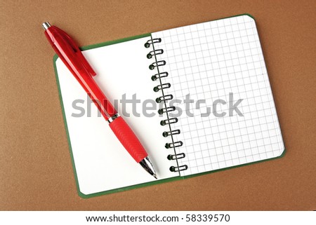 Opened notebook squared page with red pen over it on brown background