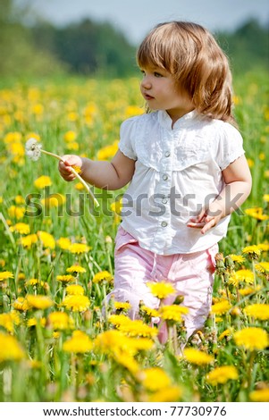 Little girl in a dandelion meadow holding dandelion