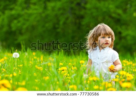 Little girl in a dandelion meadow holding dandelion blossom