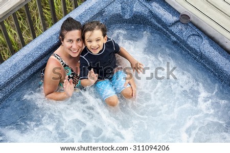 A smiling woman and child waving to the camera from a hot tub