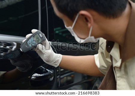 A worker inspecting car paint with a meter reading