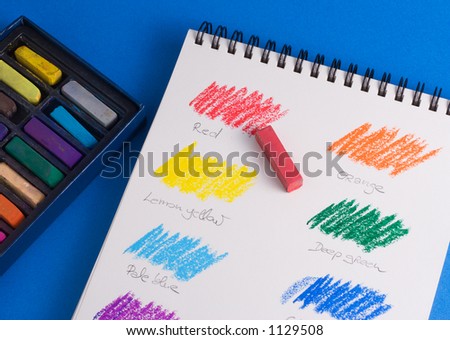Pastel color chart hand-drawn on a sketchbook, over a blue background