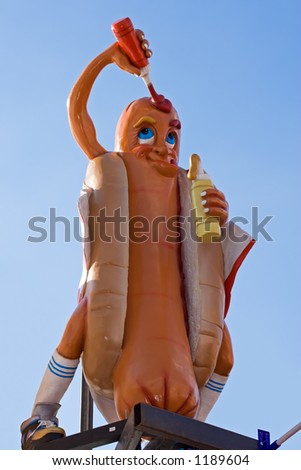 A giant cartoony hot-dog sign on the roof of a fast food shop