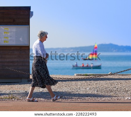 NICE, FRANCE -SEPTEMBER 27: mature woman walking beside beach with colorful boat in ocean background. September 27, 2014 in Nice, France.
